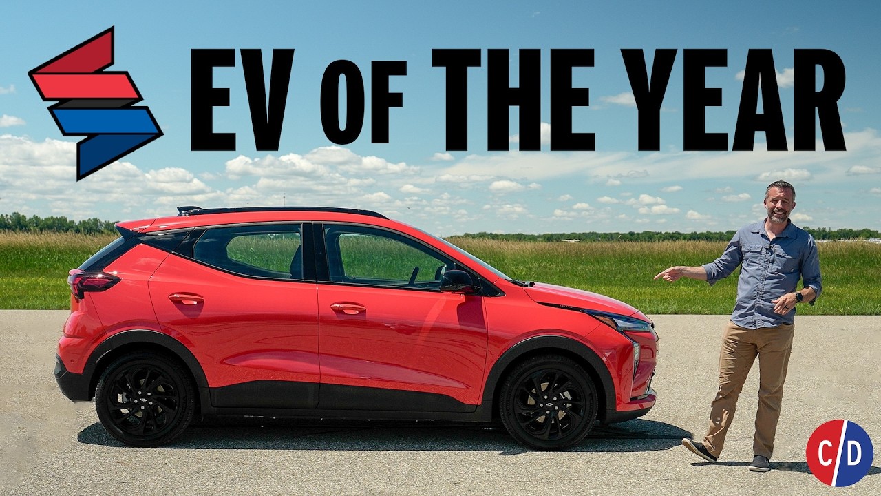 Red electric SUV with 'EV of the Year' text and man presenting vehicle in outdoor field setting