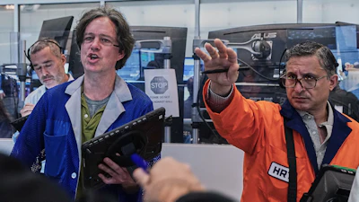 Three men demonstrate technology at an industrial event, with one wearing an HR badge and orange safety vest gesturing toward computer equipment.