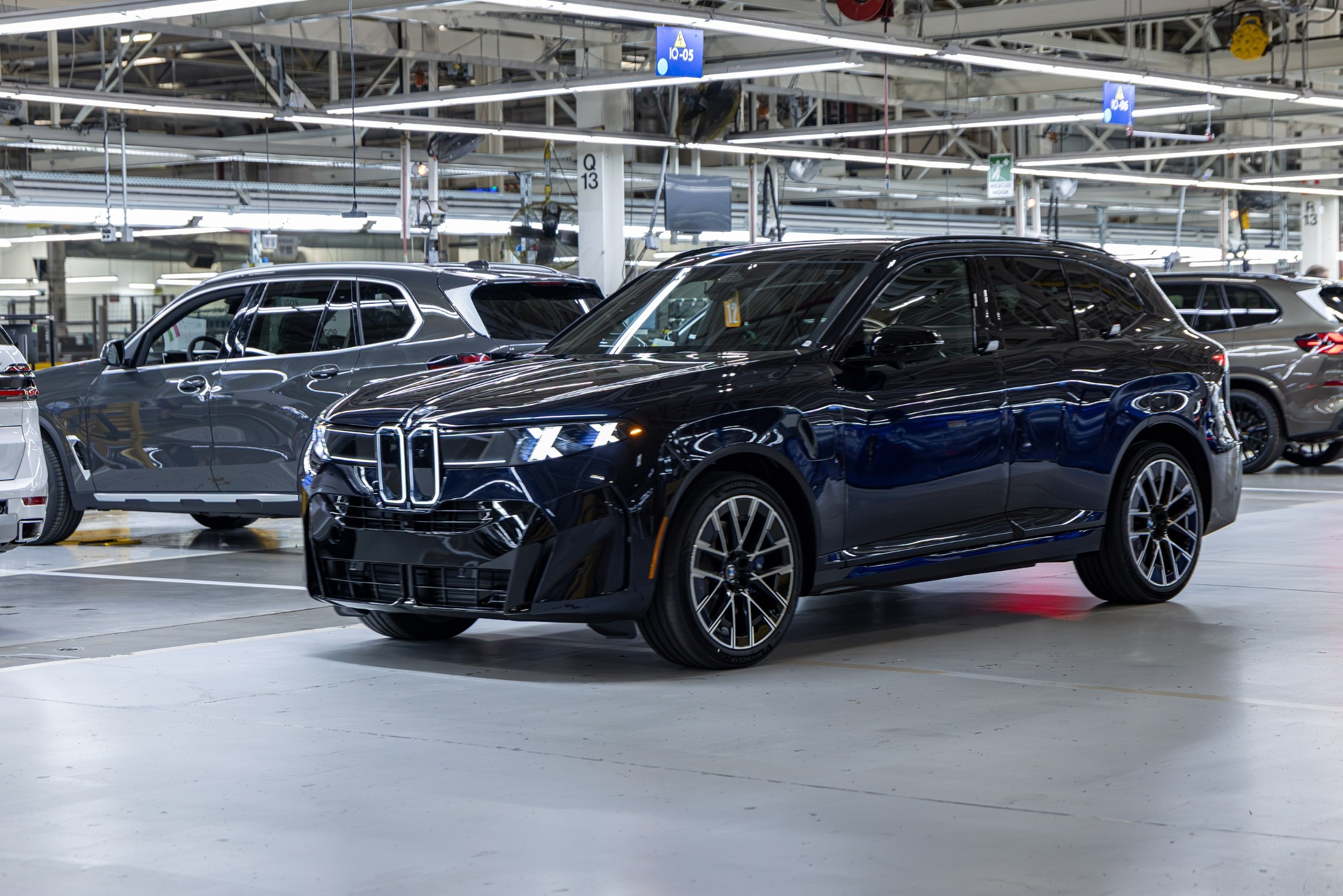 Dark blue BMW X7 luxury SUV displayed in modern manufacturing facility with industrial ceiling