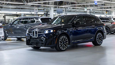 Dark blue BMW X7 luxury SUV displayed in modern manufacturing facility with industrial ceiling