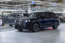 Dark blue BMW X7 luxury SUV displayed in modern manufacturing facility with industrial ceiling