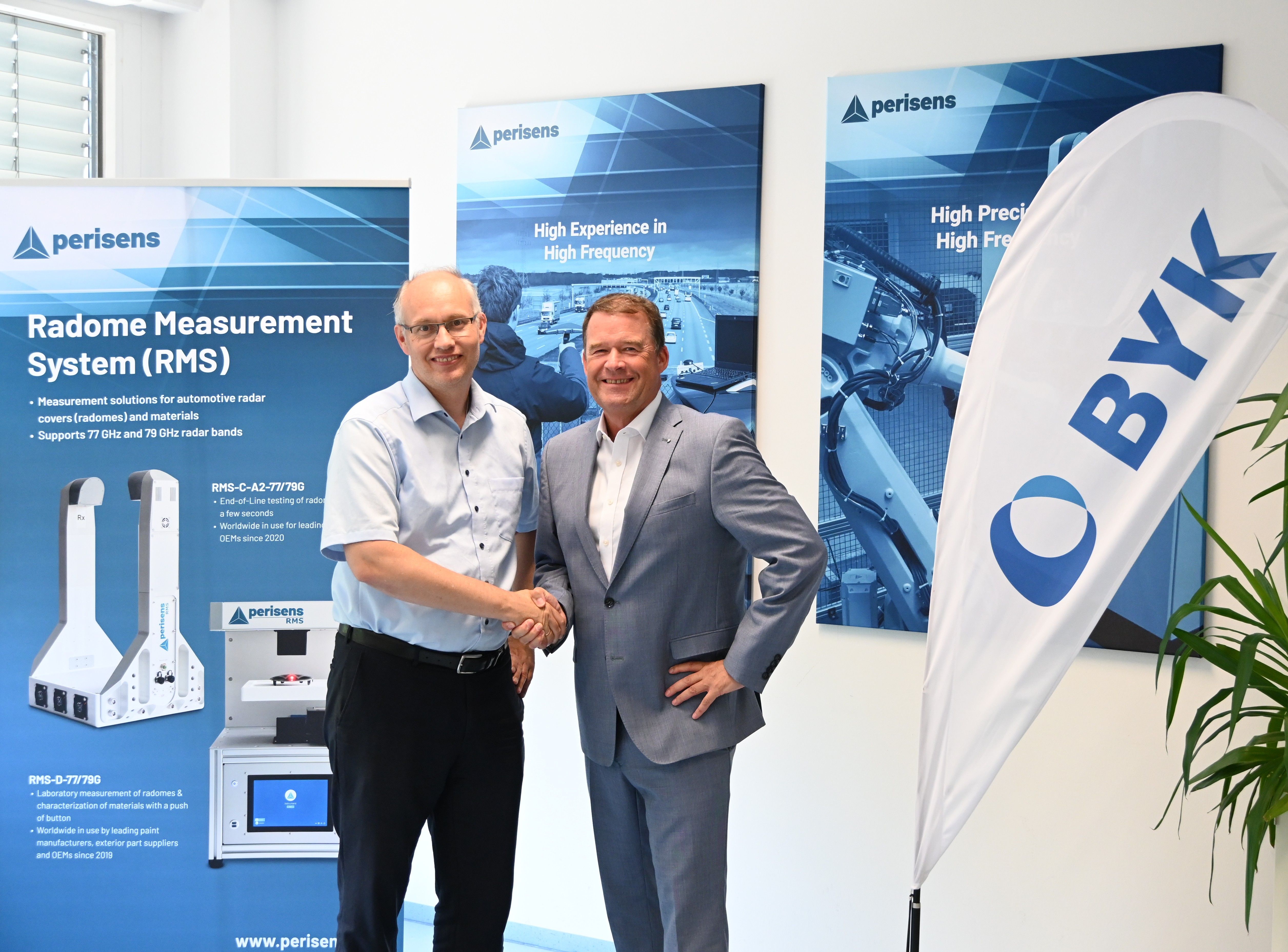 Two business professionals shaking hands at Perisens corporate event with Radome Measurement System product displays and branded banners