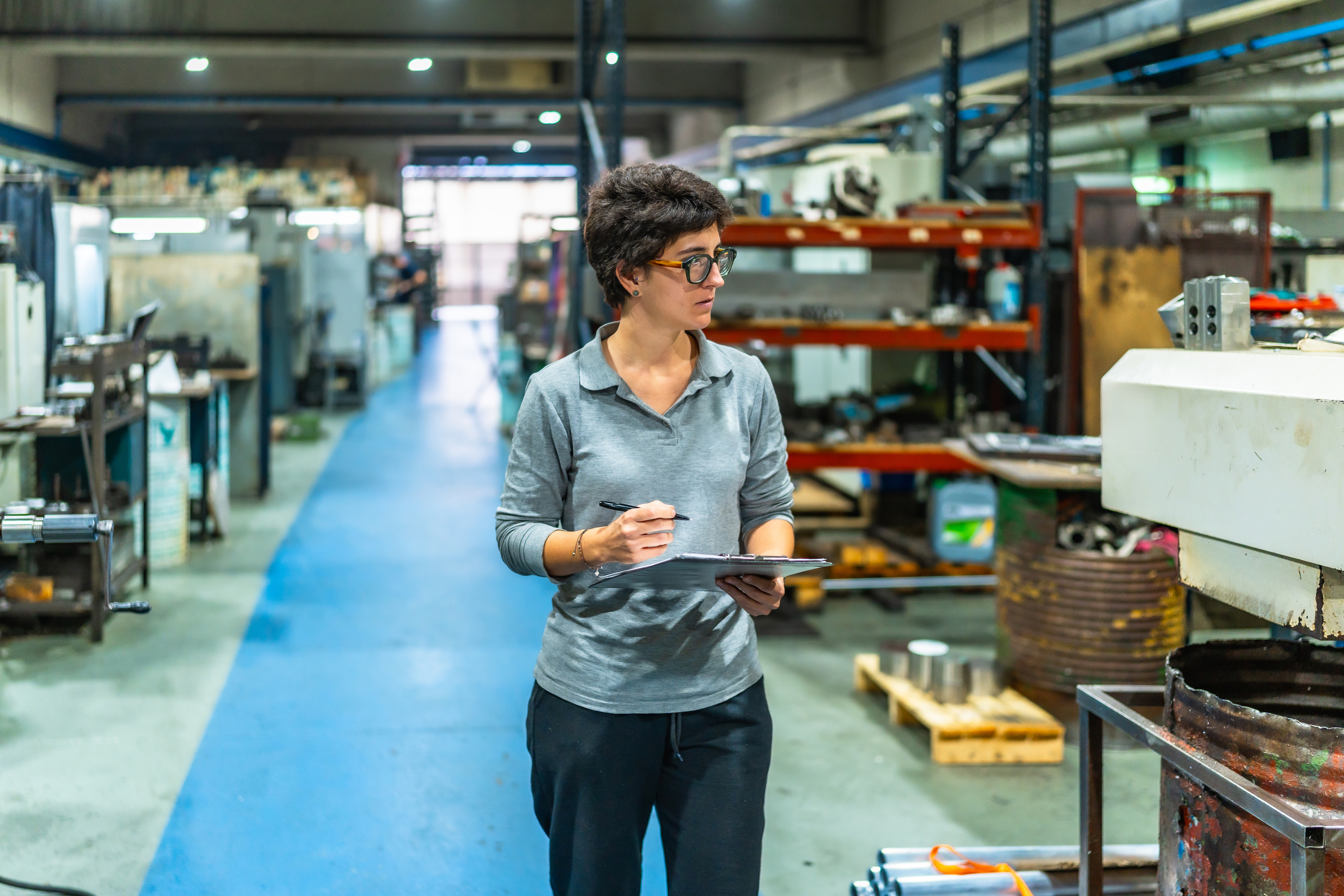 Woman in glasses holding tablet in industrial warehouse with blue floor and equipment