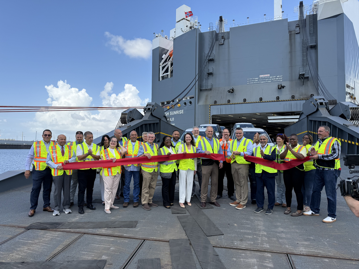 Team members in safety vests hold red ribbon at ribbon-cutting ceremony in front of industrial vessel