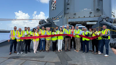 Team members in safety vests hold red ribbon at ribbon-cutting ceremony in front of industrial vessel