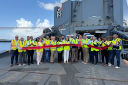 Team members in safety vests hold red ribbon at ribbon-cutting ceremony in front of industrial vessel
