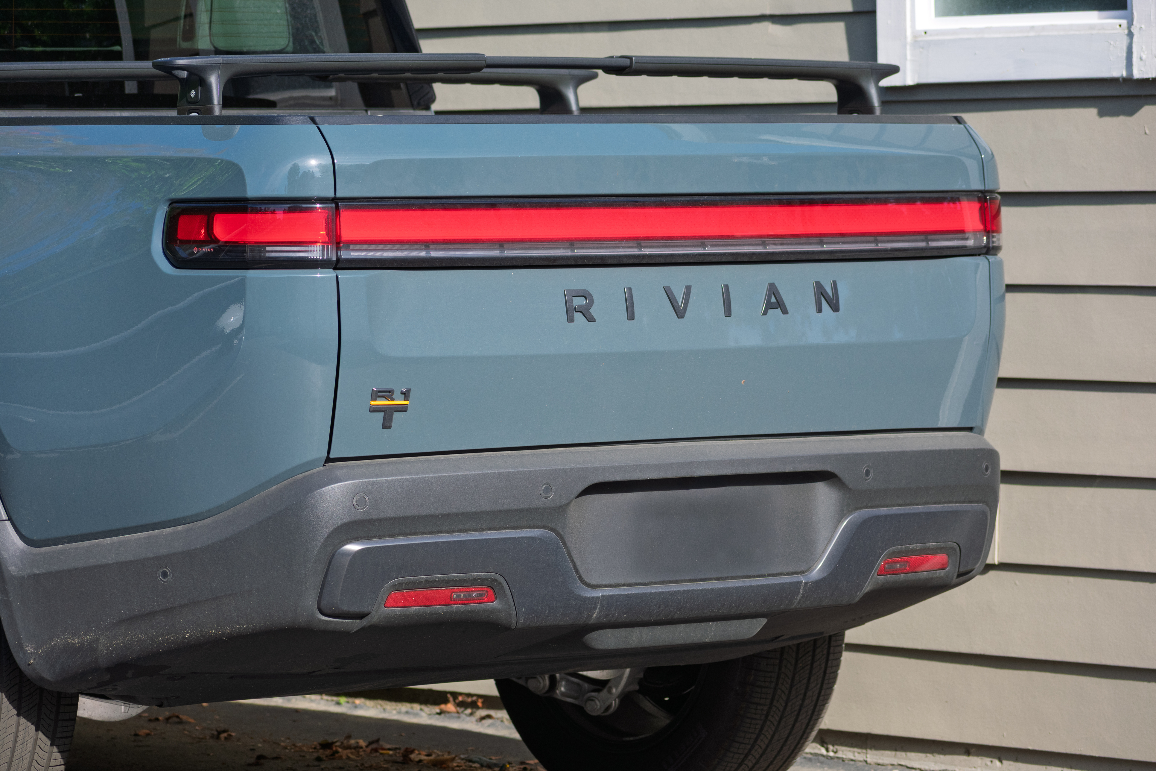 Rear view of light blue Rivian electric truck with red LED taillight and gray bumper