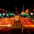 Night traffic intersection with red vehicle light trails, illuminated street signs, and photo enforcement sign at urban crossroads