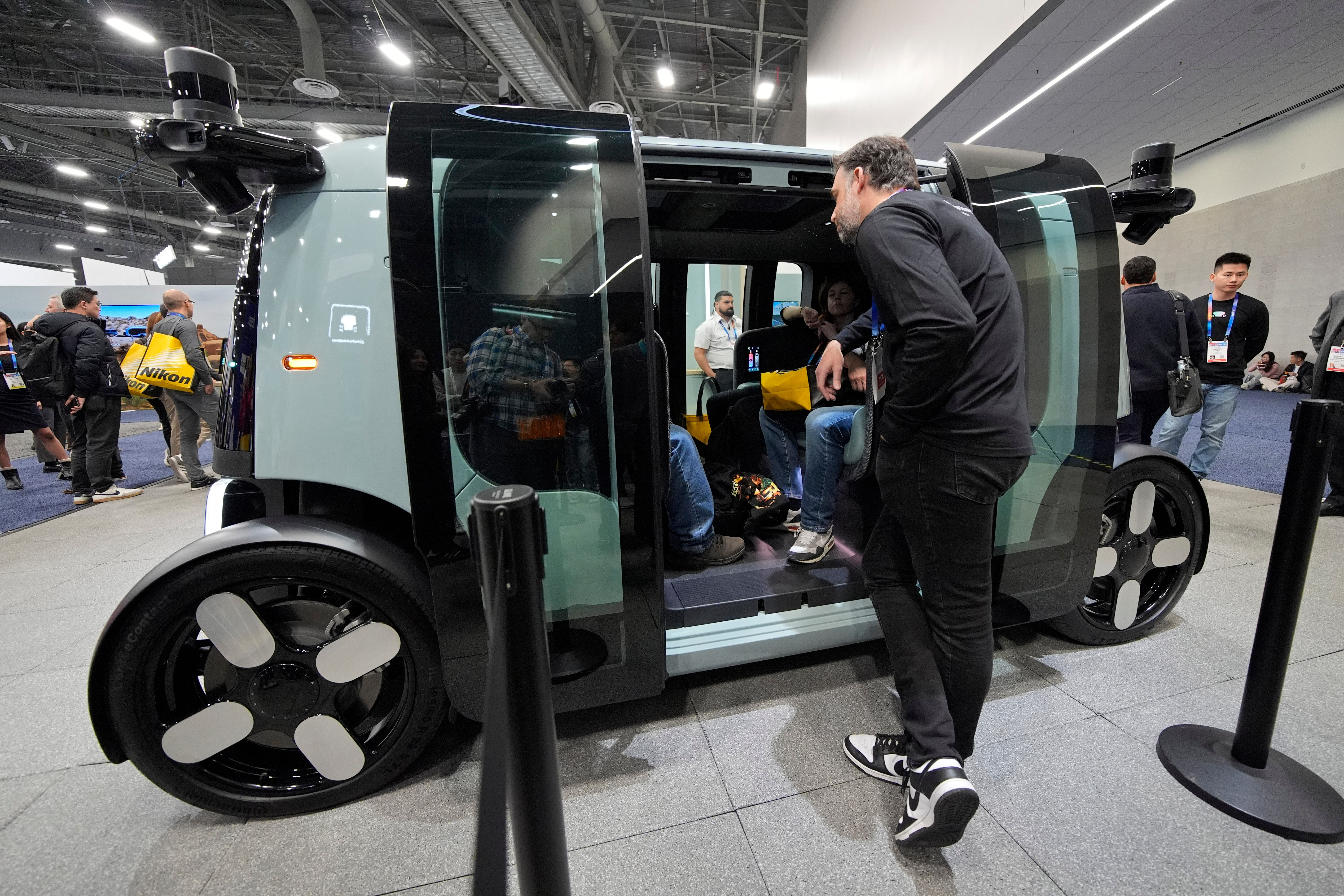 Futuristic autonomous delivery vehicle on display at tech conference with visitors and staff observing