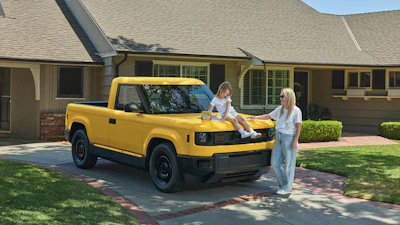 Woman and child with yellow compact truck in residential driveway on sunny day