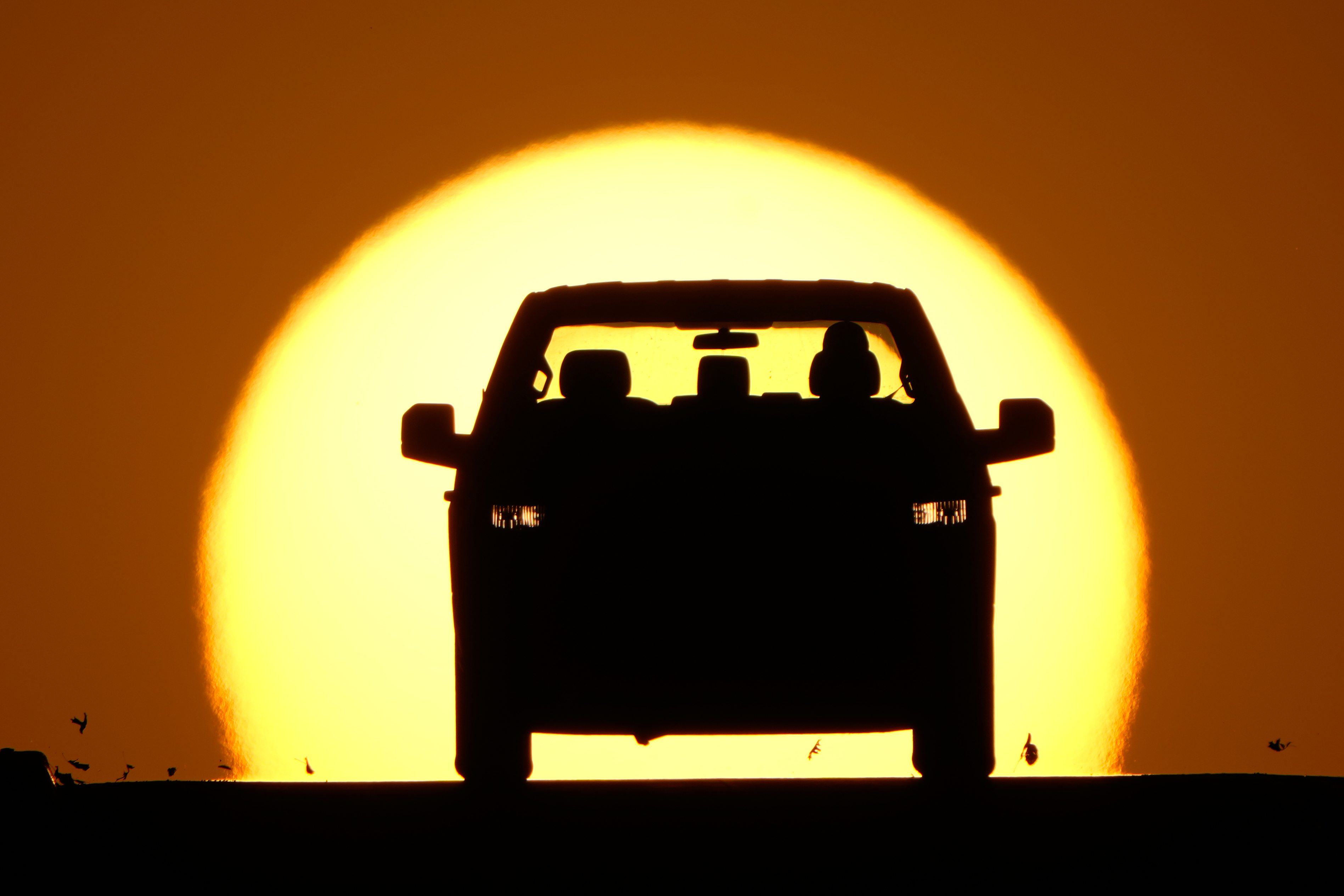 Car silhouette against a large golden sunset sky
