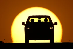 Car silhouette against a large golden sunset sky