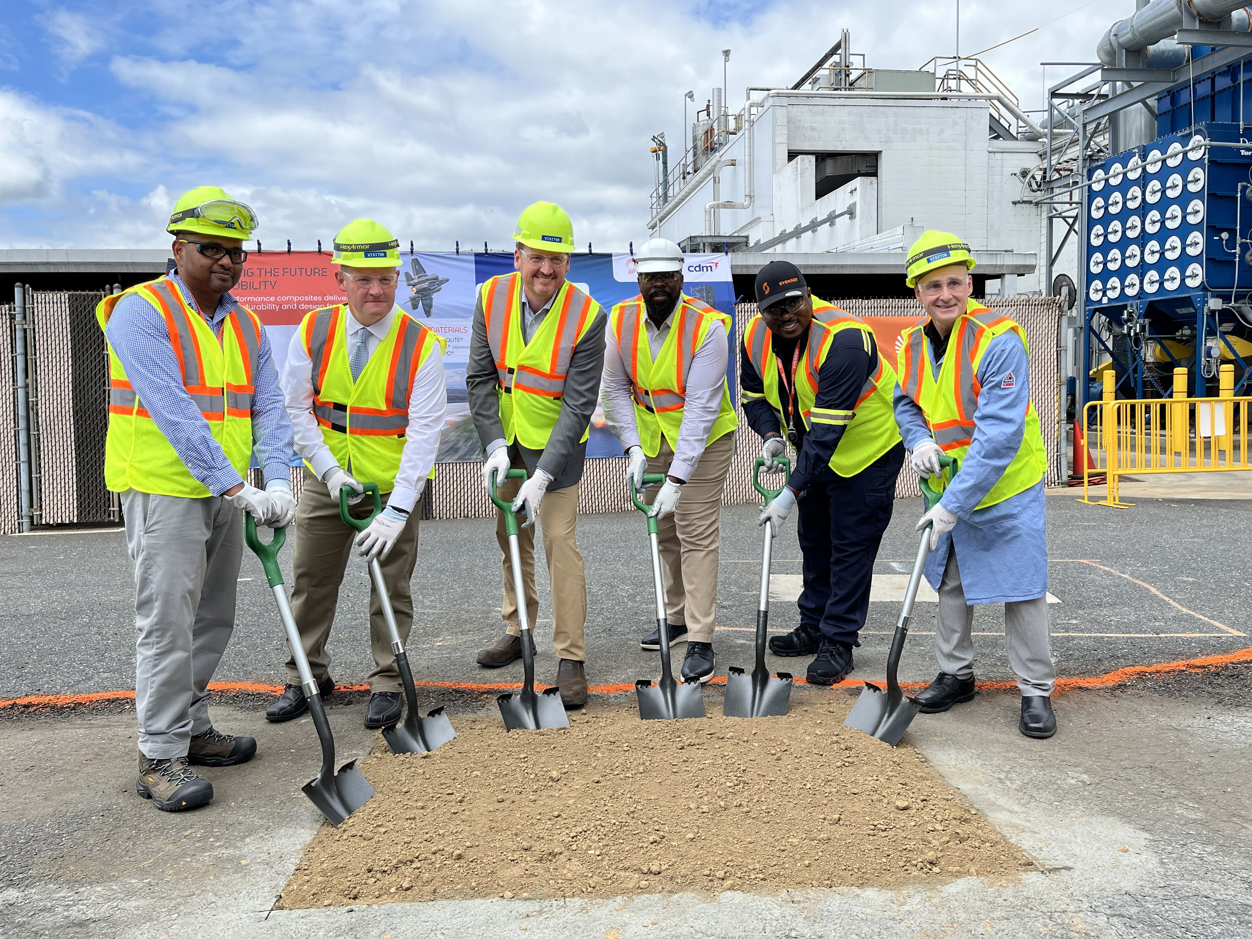 Construction workers in safety vests and hard hats break ground at industrial facility with shovels