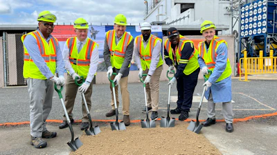 Construction workers in safety vests and hard hats break ground at industrial facility with shovels