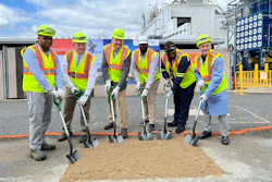 Construction workers in safety vests and hard hats break ground at industrial facility with shovels