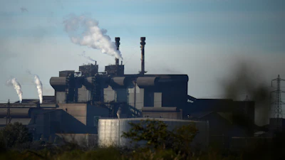 Industrial steel mill facility with multiple smokestacks emitting steam against a blue sky
