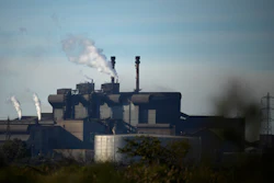 Industrial steel mill facility with multiple smokestacks emitting steam against a blue sky