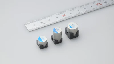 Three surface-mount electronic components with blue labels displayed next to a measuring ruler for size comparison