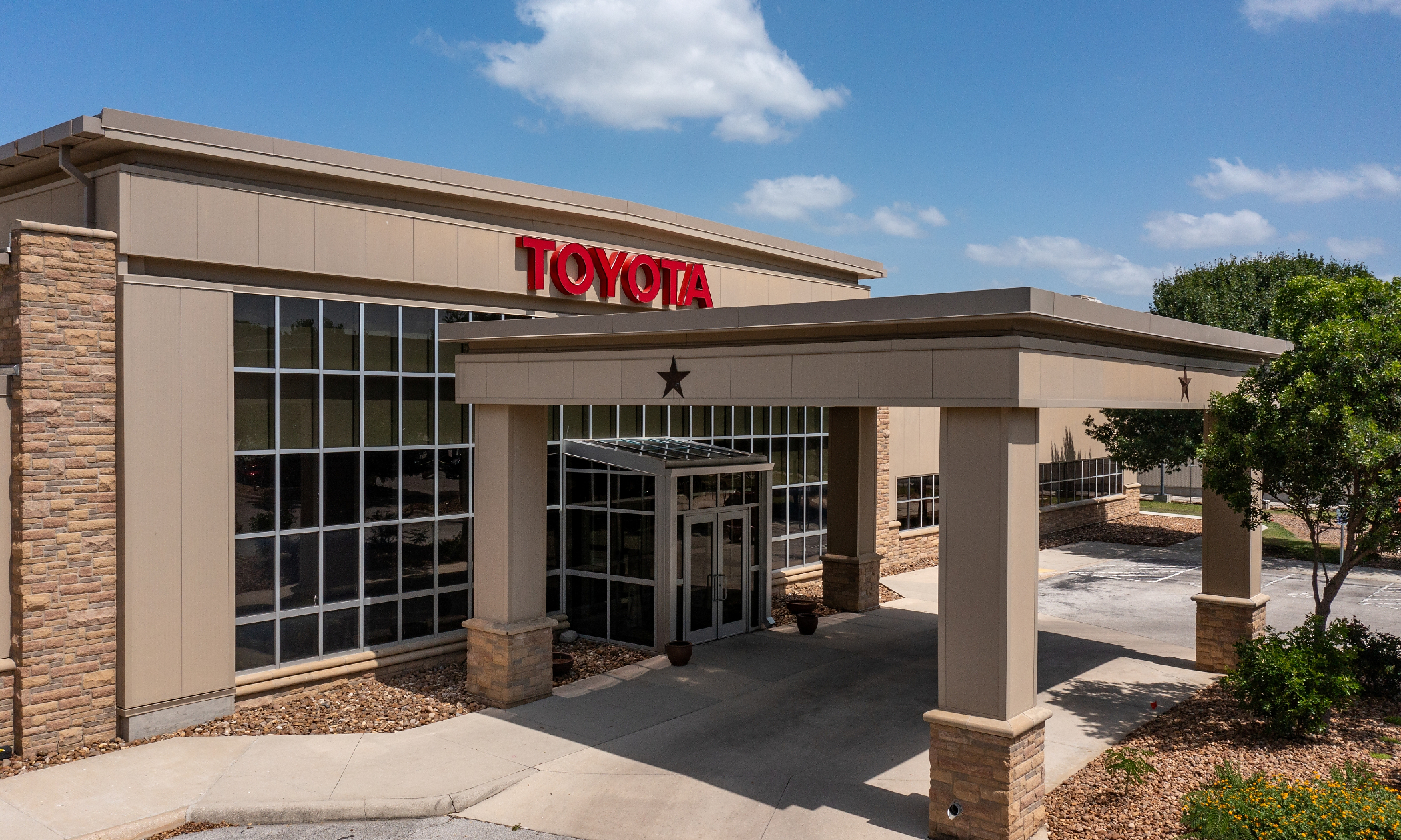 Toyota dealership storefront with red signage, brick and tan exterior, covered entrance, and landscaping