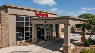 Toyota dealership storefront with red signage, brick and tan exterior, covered entrance, and landscaping