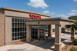 Toyota dealership storefront with red signage, brick and tan exterior, covered entrance, and landscaping