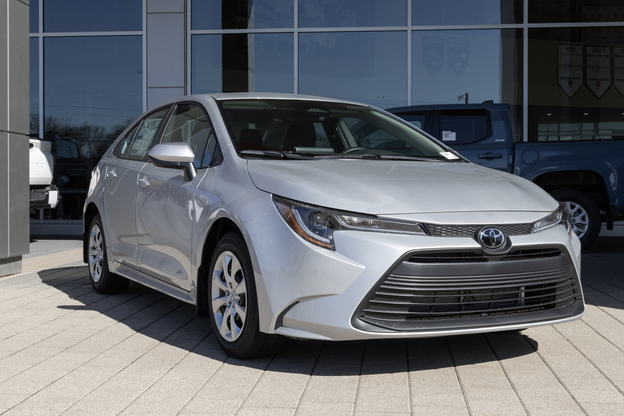 Silver Toyota Corolla sedan parked at dealership with glass storefront backdrop