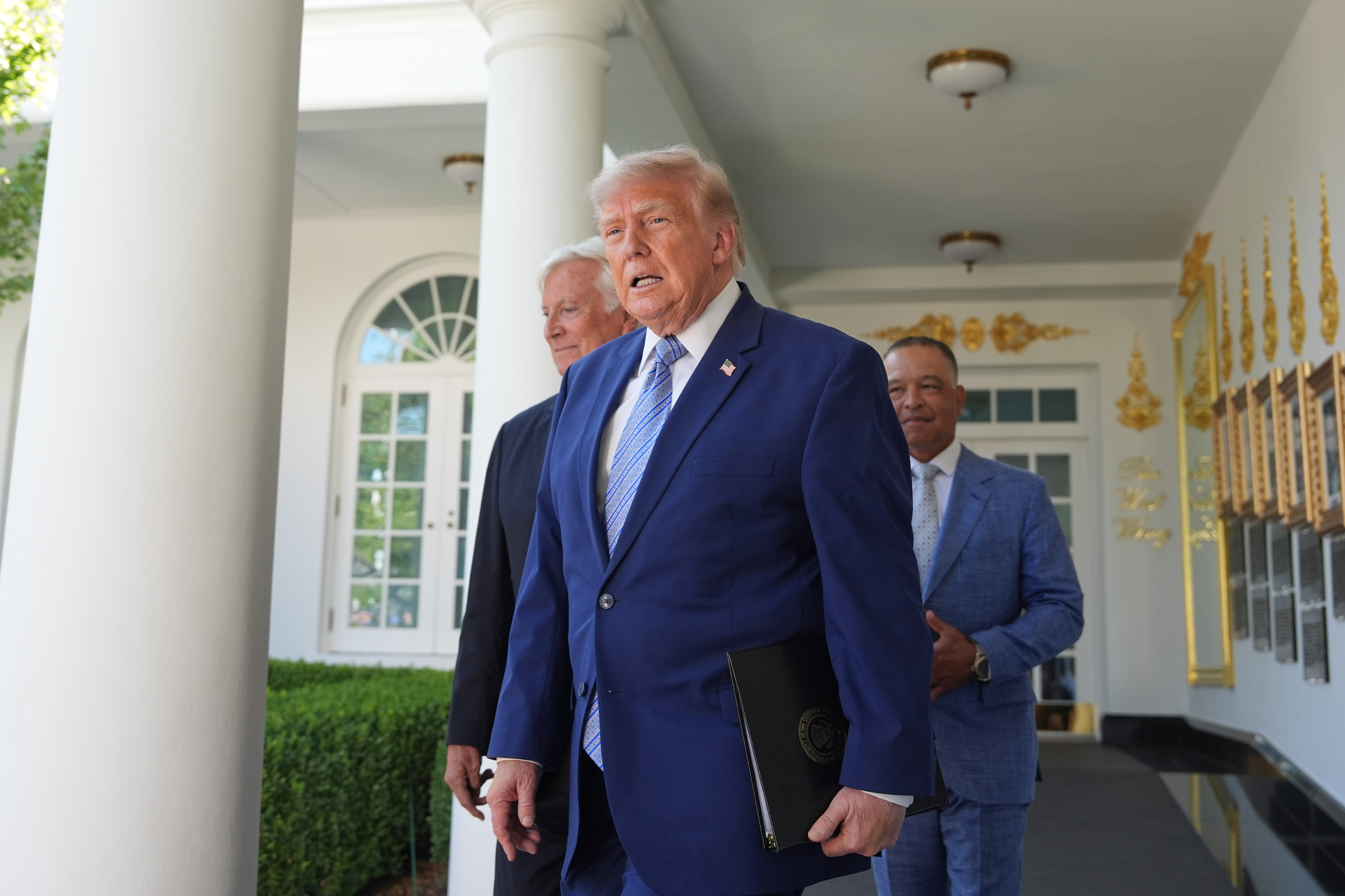 Three men in business suits walking through a white columned corridor with decorative gold accents