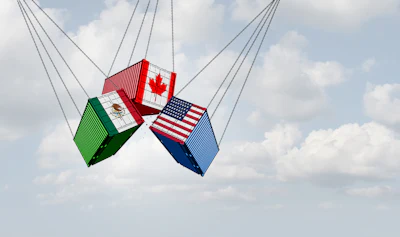 Three shipping containers decorated with Canadian, Mexican, and American flags suspended by cables against a blue sky