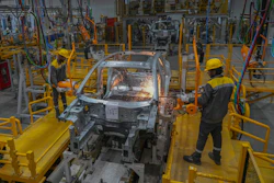 Automotive manufacturing facility with welding robot performing metal work on vehicle body frame