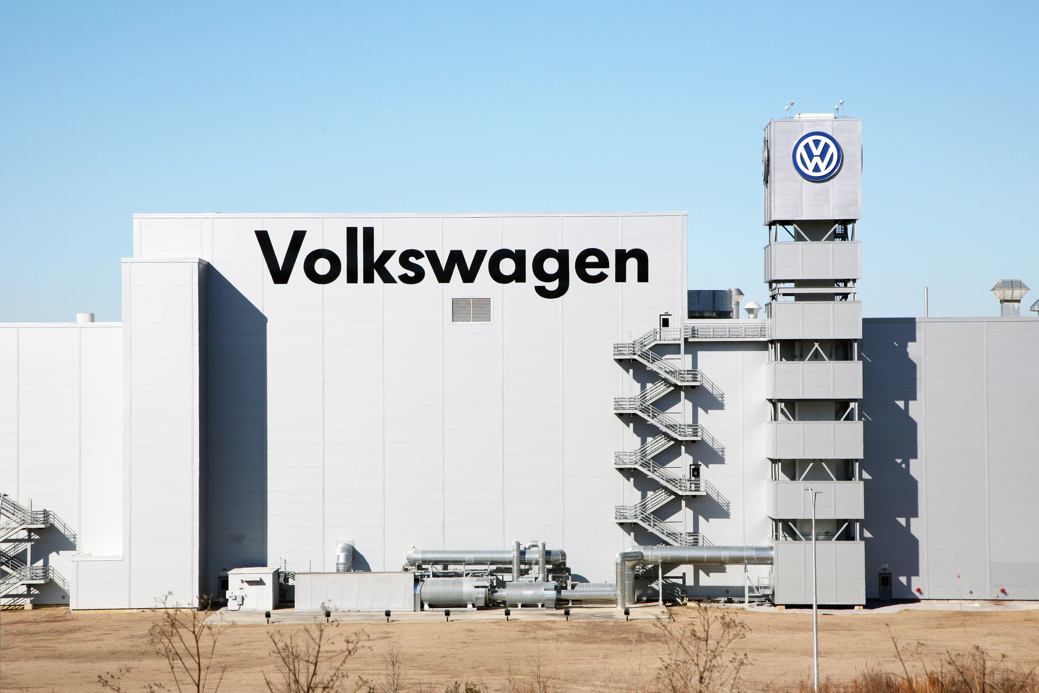 Volkswagen manufacturing facility with white building, company signage, and branded tower against clear blue sky
