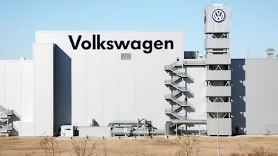 Volkswagen manufacturing facility with white building, company signage, and branded tower against clear blue sky