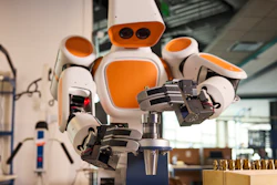 Orange and white humanoid robot with articulated hands in a workshop laboratory setting