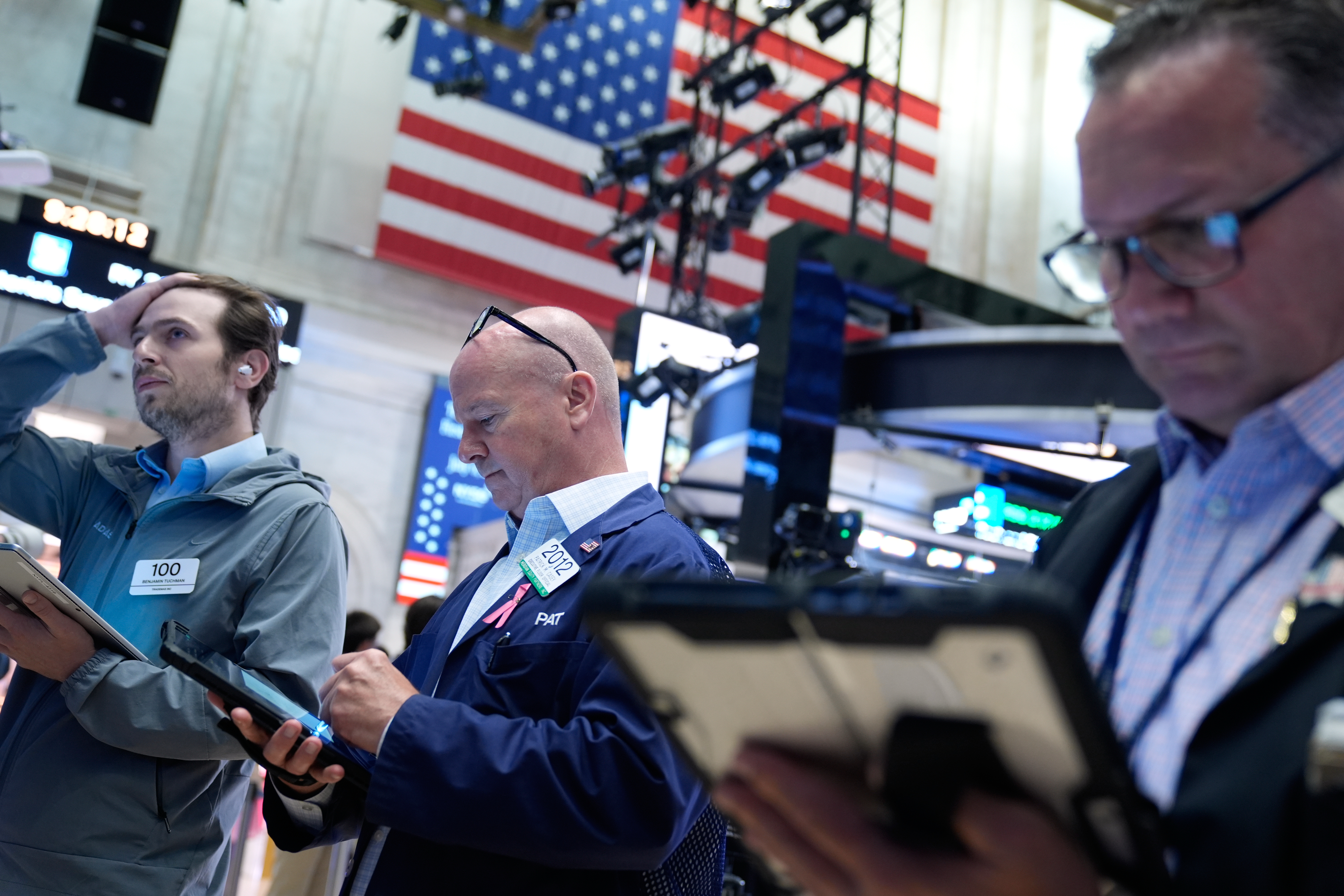 Three traders monitor financial markets at stock exchange with American flag backdrop