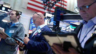 Three traders monitor financial markets at stock exchange with American flag backdrop