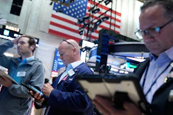 Three traders monitor financial markets at stock exchange with American flag backdrop