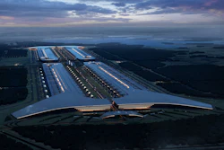 Aerial view of large industrial facility with parallel illuminated sections at twilight, surrounded by forests and fields