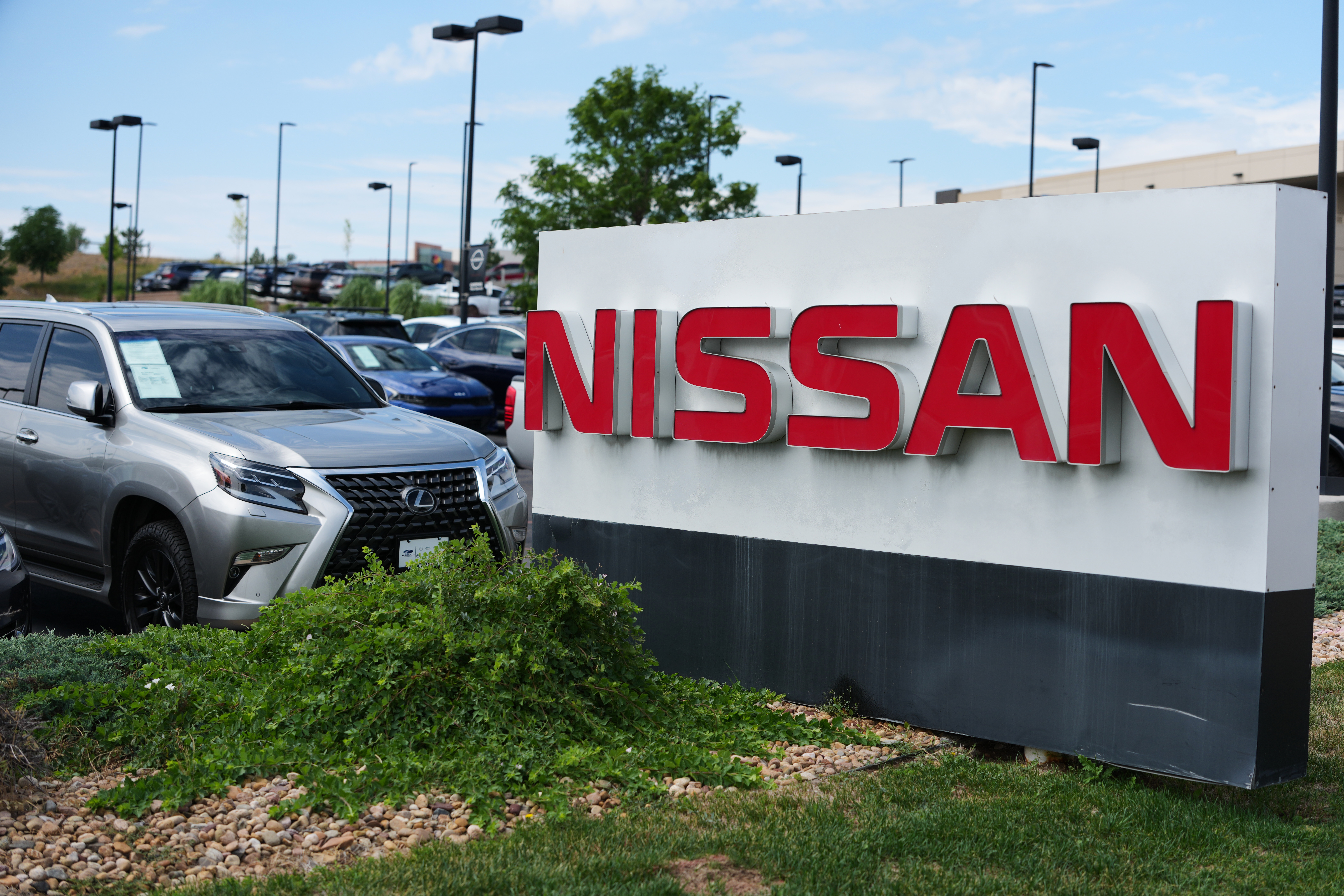 Nissan dealership sign with red lettering in outdoor parking lot with vehicles