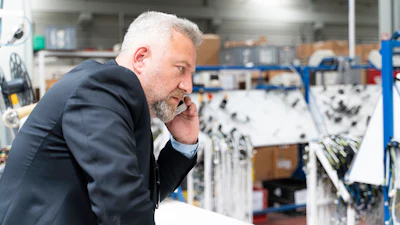 Businessman in navy blazer examining equipment in industrial warehouse facility