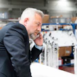 Businessman in navy blazer examining equipment in industrial warehouse facility