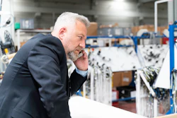 Businessman in navy blazer examining equipment in industrial warehouse facility