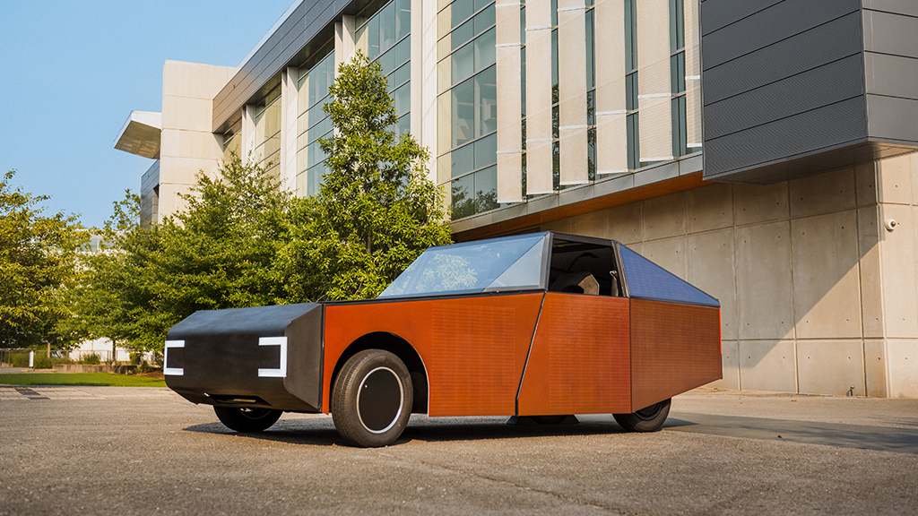 Orange and black concept vehicle with geometric design parked in front of modern building