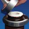 Hand pouring coconut milk from a bottle into a fresh coconut half against blue background