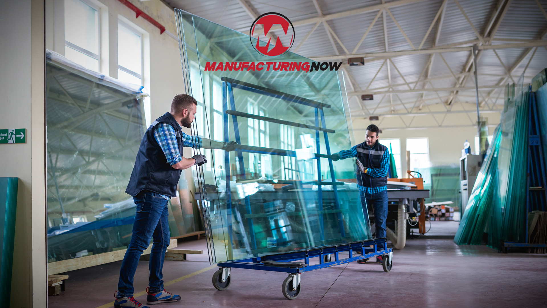 Manufacturing Now logo displayed above workers handling glass panels in industrial warehouse facility