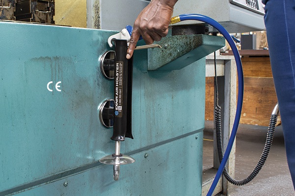 Worker operating hydraulic gauge valve on turquoise industrial machinery with blue hose attachment