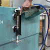 Worker operating hydraulic gauge valve on turquoise industrial machinery with blue hose attachment