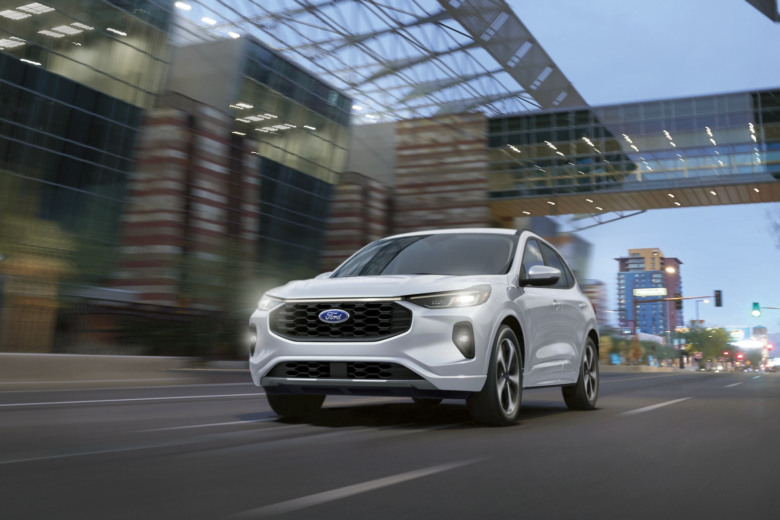 White Ford electric SUV driving through urban street with modern buildings and overpass