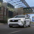 White Ford electric SUV driving through urban street with modern buildings and overpass