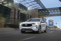 White Ford electric SUV driving through urban street with modern buildings and overpass