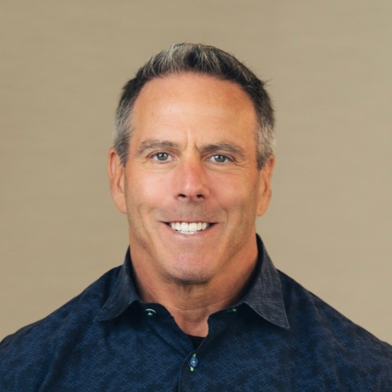 Professional headshot of a middle-aged man with gray hair wearing a dark blue shirt, smiling against a neutral background Headshot