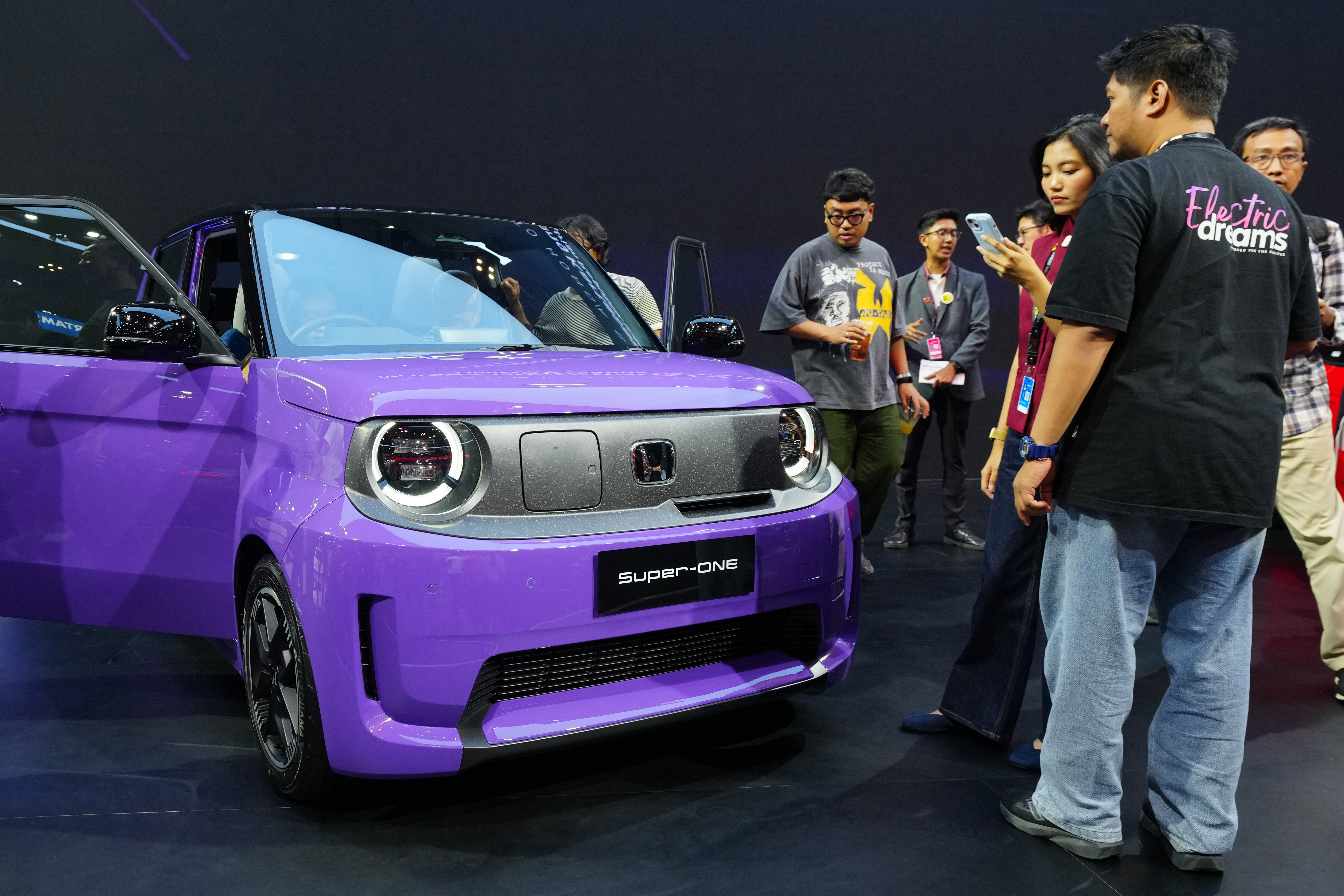 Purple Honda Super One electric vehicle on display at auto show with visitors examining the compact city car